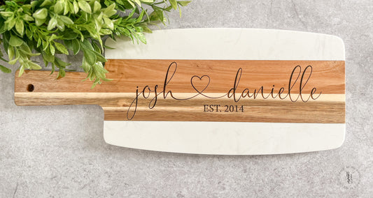 Marble and acacia wood serving board engraved with two names, a heart, and an established year.